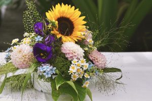 Arreglo floral con un girasol prominente, rodeado de flores en tonos suaves y vivos, simbolizando la vida, el recuerdo y la esperanza