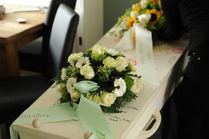 Elegante arreglo floral de tonos blancos y verdes sobre una caja de madera con escrituras, reflejando condolencias y memorias